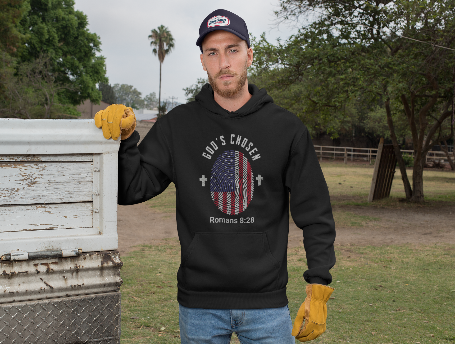 Man wearing a black hoodie with a graphic design, standing next to a beehive in an outdoor setting.