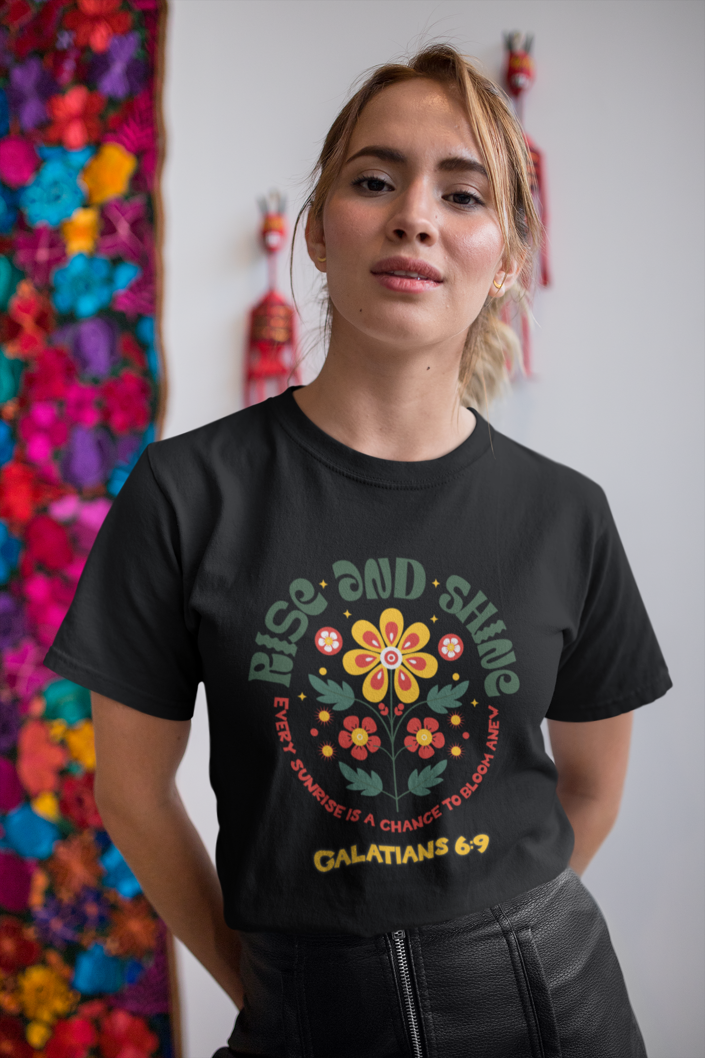 Woman wearing a black t-shirt with a colorful floral design and text, standing in front of a colorful floral wall.