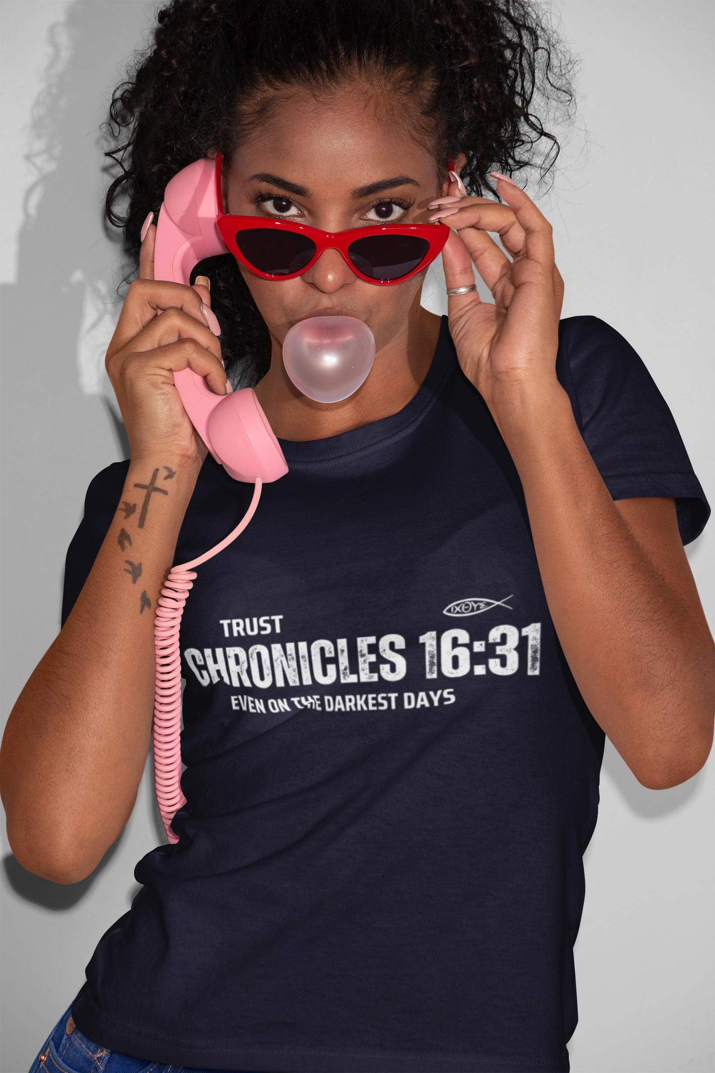 Person wearing a black t-shirt with text, holding a pink phone to their ear, blowing a bubble of gum.