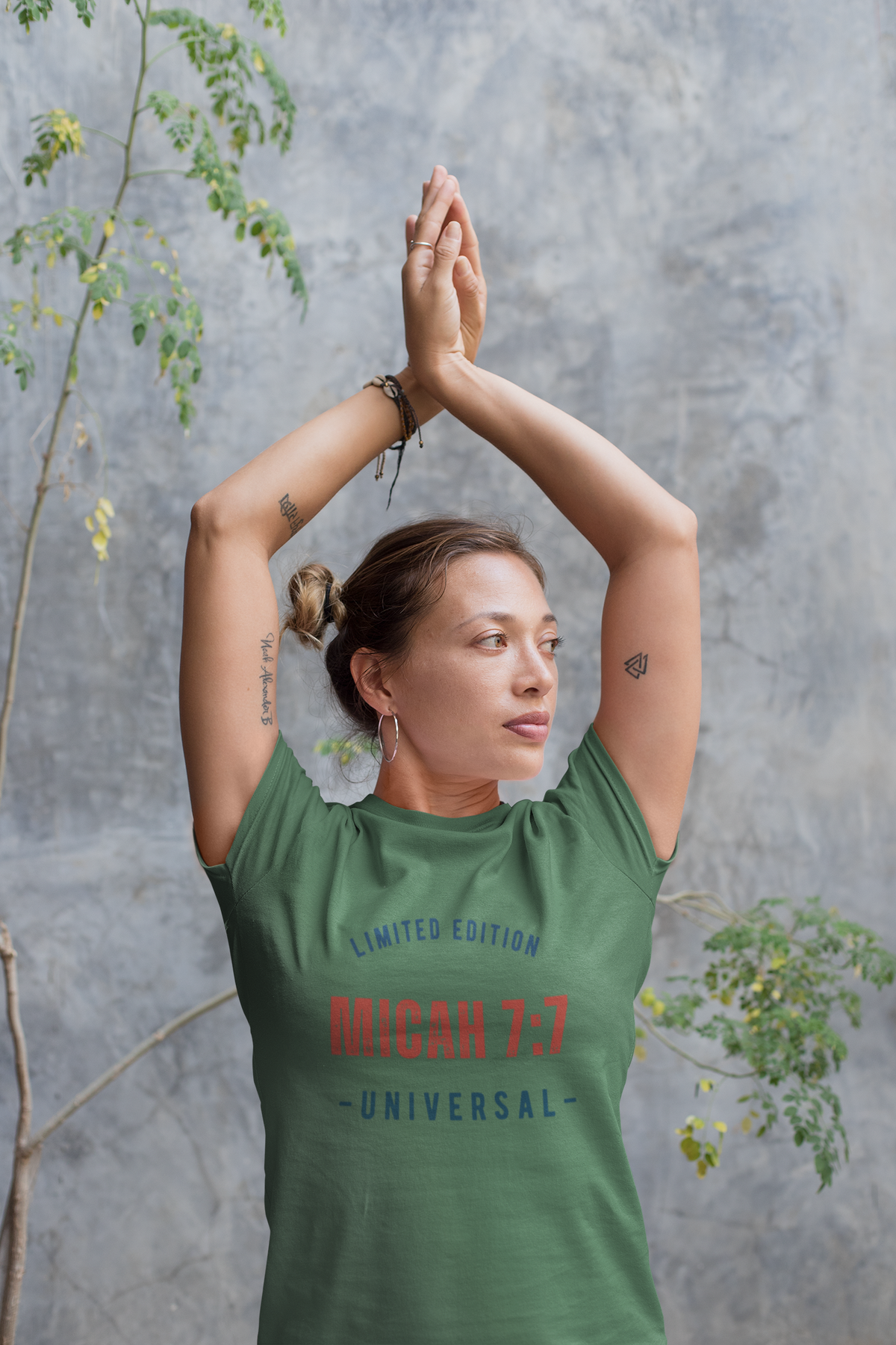 Person wearing a green t-shirt with text, standing against a gray wall with plants.