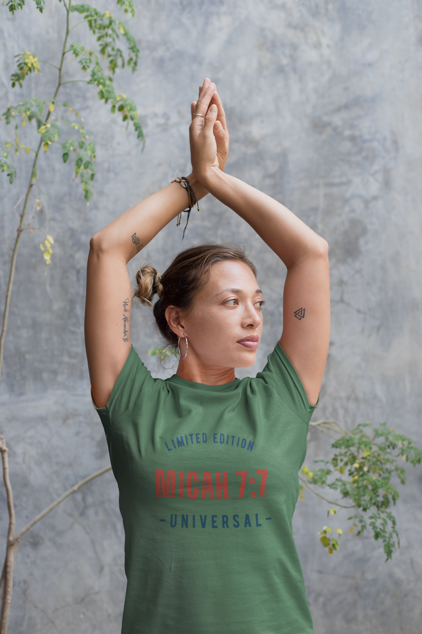Person wearing a green t-shirt with text, standing against a gray wall with plants.