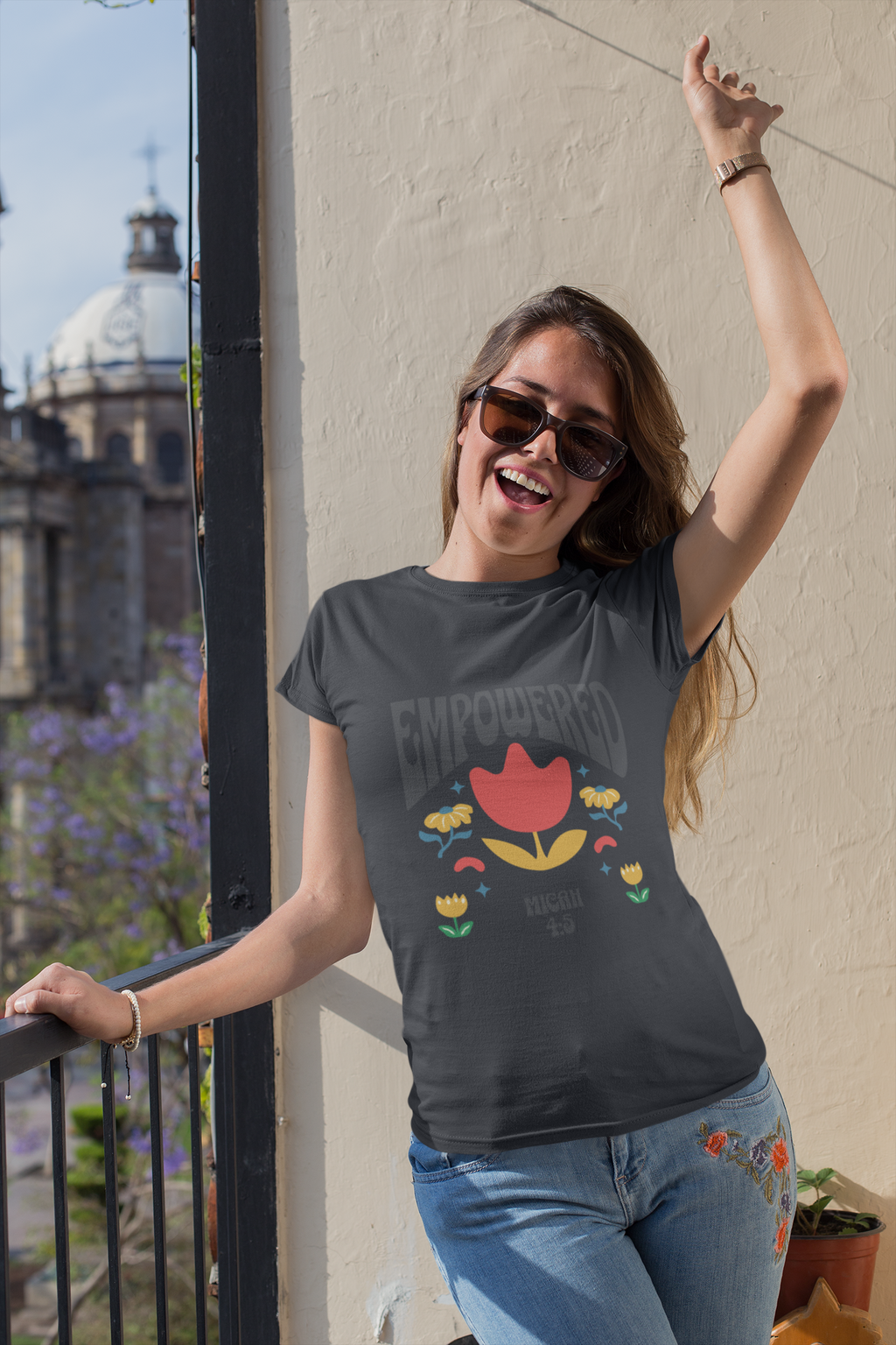 Woman wearing a 'Empowered' t-shirt with a colorful design, standing on a balcony.