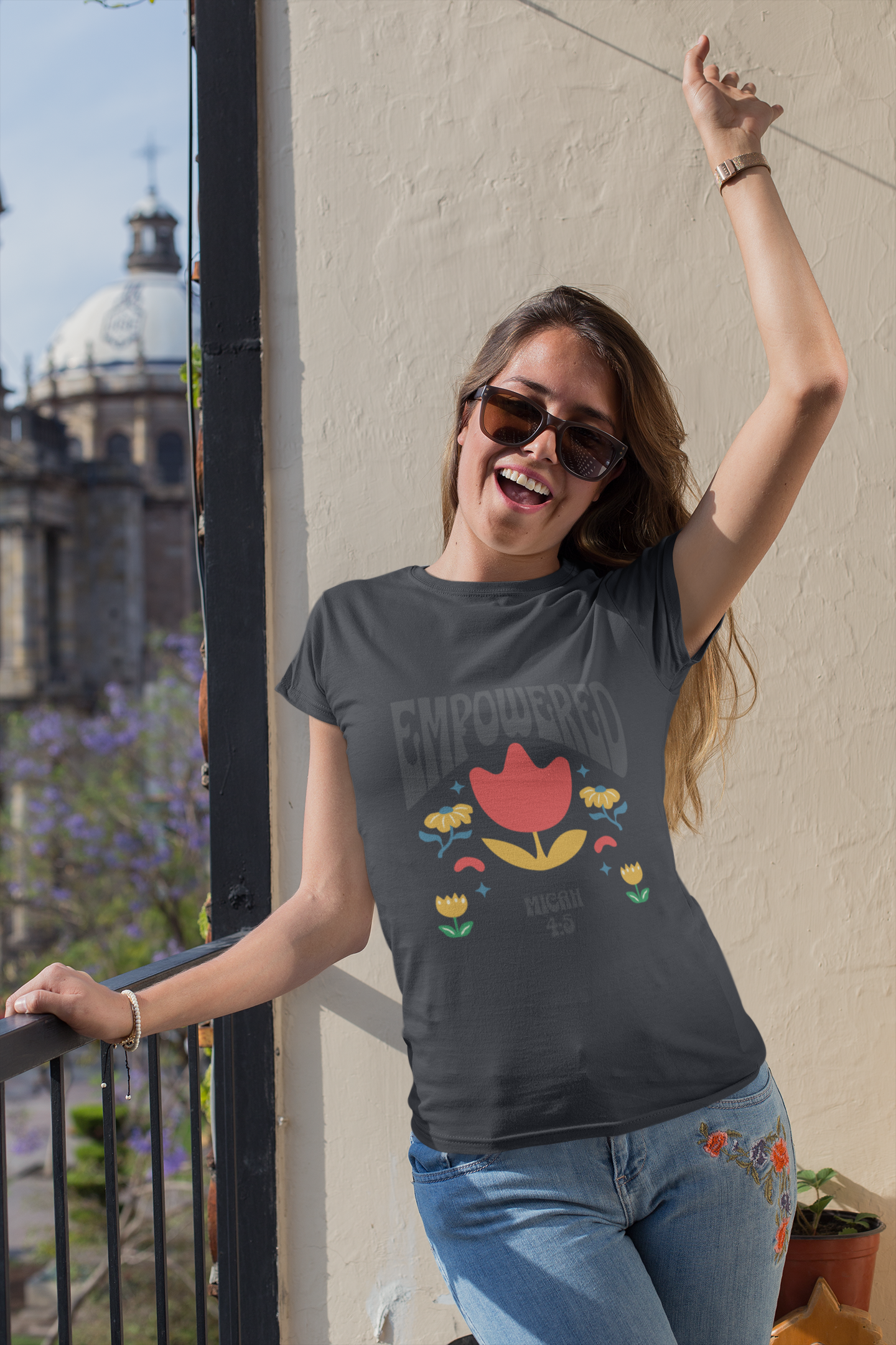 Woman wearing a 'Empowered' t-shirt with a colorful design, standing on a balcony.