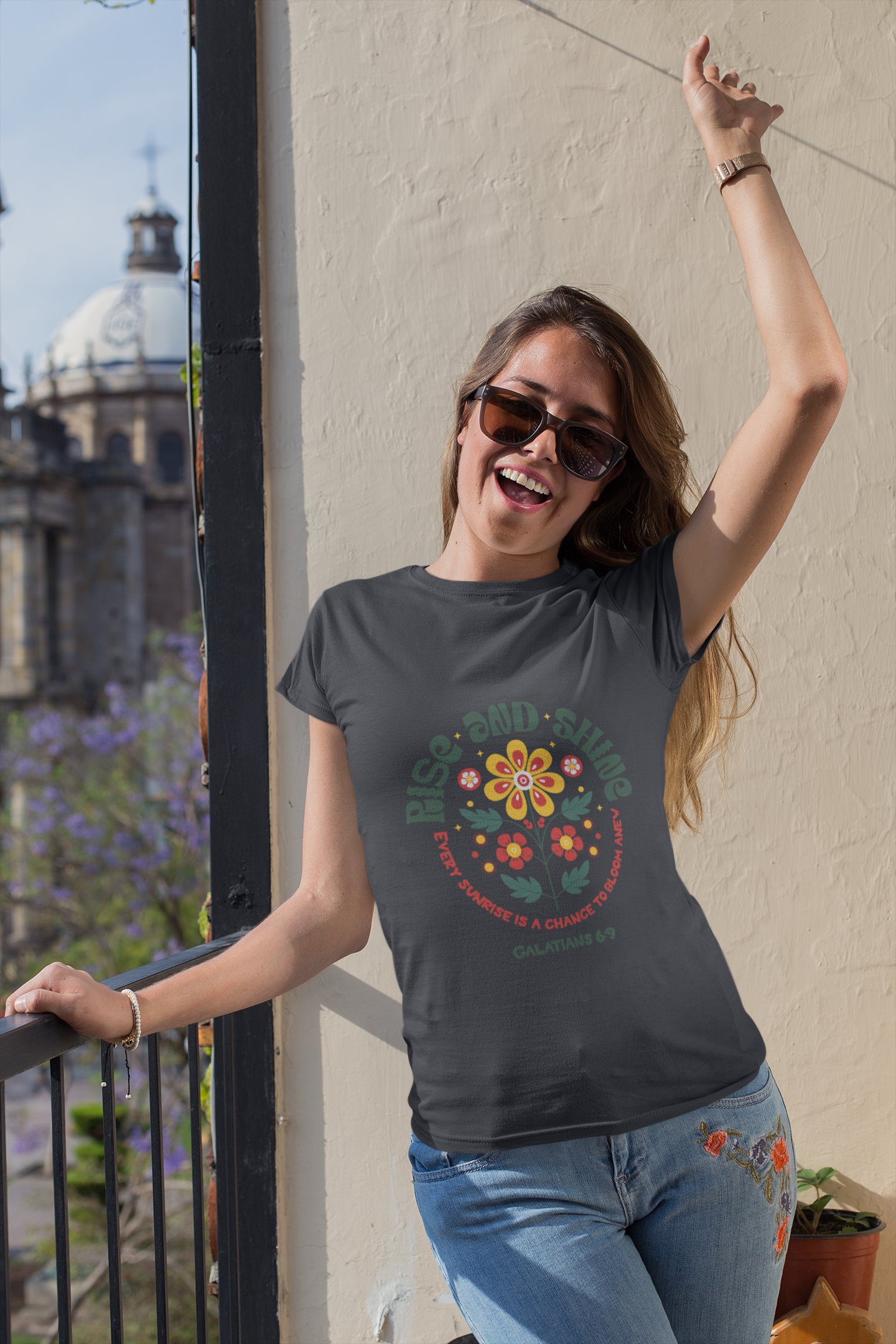 Woman wearing a t-shirt with a colorful design, standing on a balcony with a cityscape background.